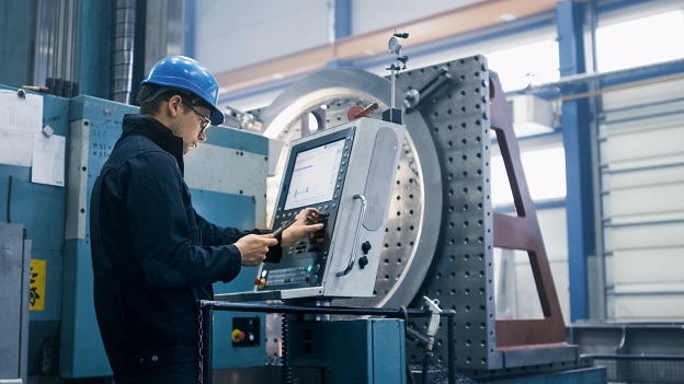 Factory worker is programming a CNC milling machine with a tablet computer