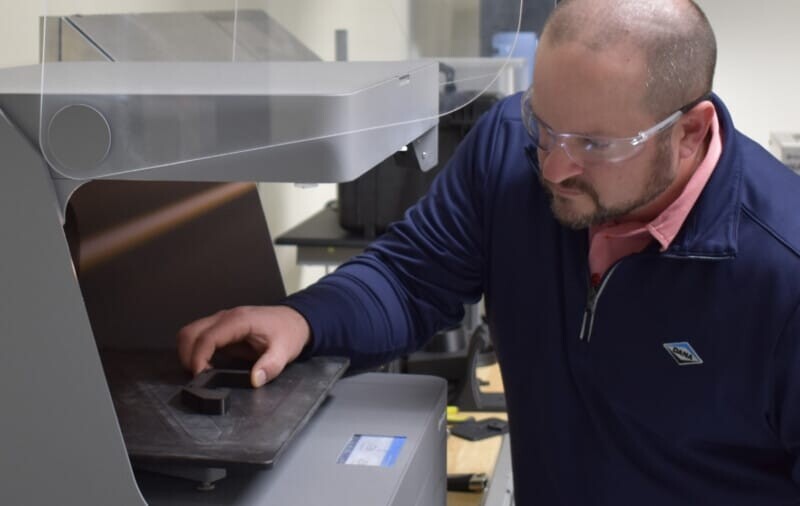 A man 3D printing a custom part on a Markforged industrial printer.