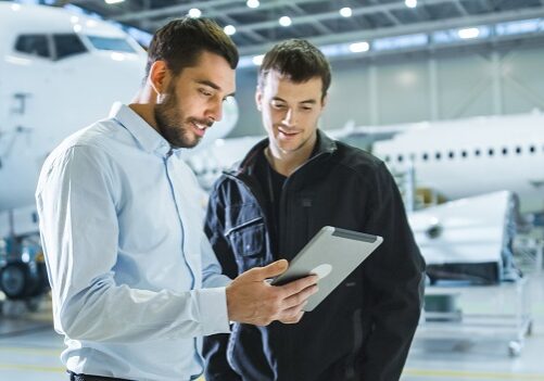 Two men in airplane hanger talking and looking at a tablet